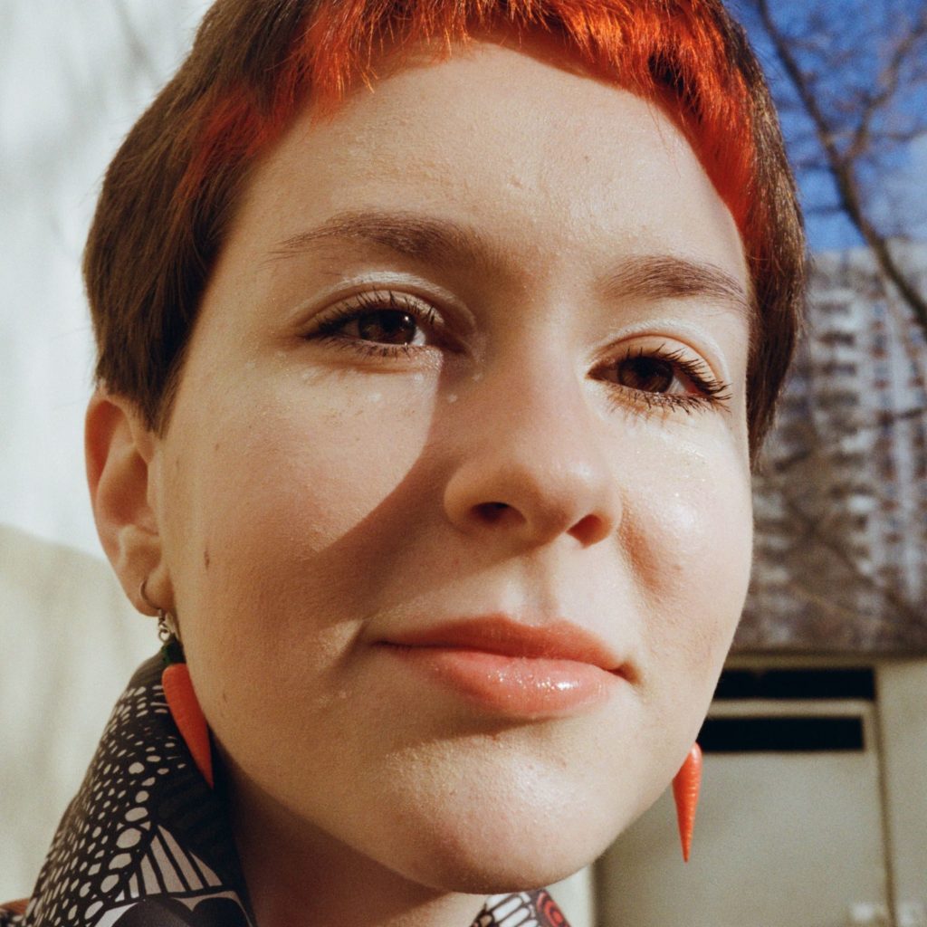 o nas Crop pensive young female with short red hair chilling on street and looking at camera